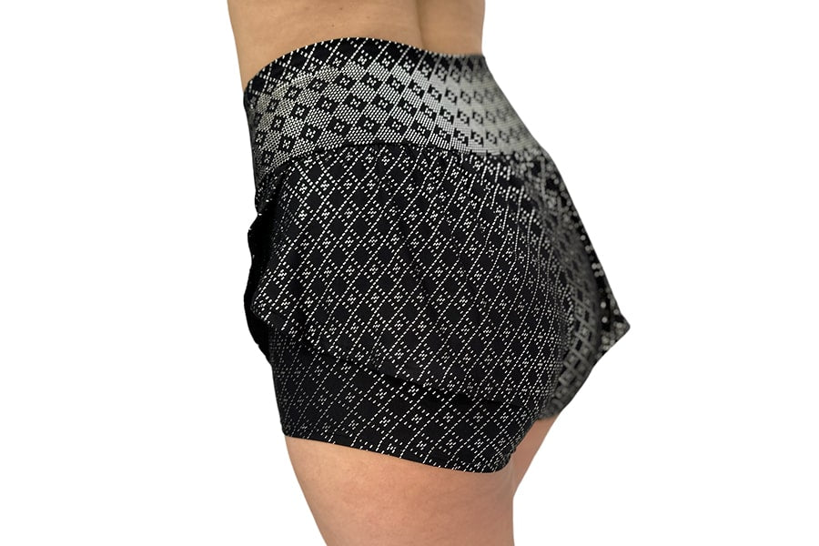 A person models the Angela Ruffle Short by Melodia Designs—a high-waisted, black and gray short with a bold geometric diamond pattern and elastic-free waistband—shown from the side against a white background.