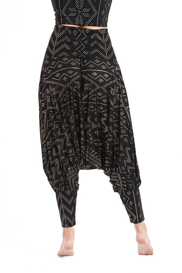 A models barefoot lower body is shown on a white background, wearing the Christine Luxor Harem Jumper by Melodia Designs—black harem pants featuring gold geometric patterns.