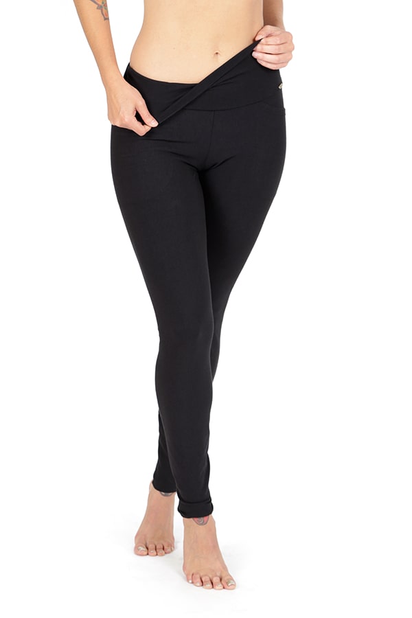 A person models Melodia Designs Elsa Pocket Legging, featuring a high-rise foldable waistband, standing barefoot against a white background and slightly pulling down the band to display its fit. Their face remains unseen.