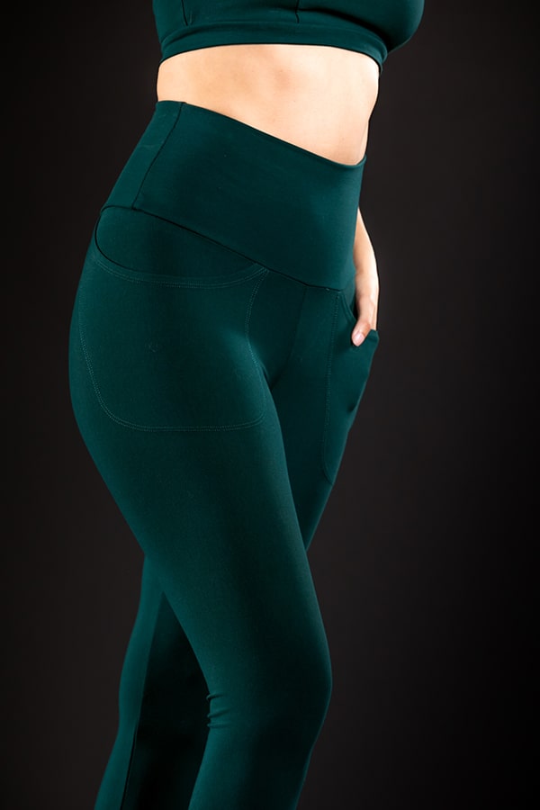 A person models the Melodia Designs Elsa Pocket Legging Malachite, featuring a high-rise waistband and pockets, paired with a matching crop top, standing against a black background.