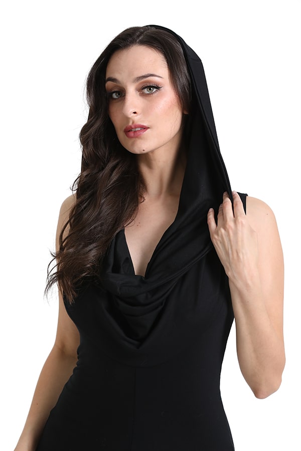A woman with long brown hair models the Melodia Designs Leeloo Romper, a sleeveless black eco-luxe style with a cowled hood, holding the hood’s edge as she poses against a white background.