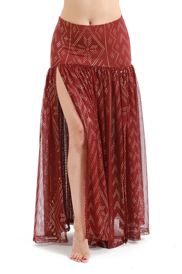 A barefoot person wears the Melodia Designs Golden Skirt Luxor, showcasing its high slit, sheer geometric overlay, and versatile waistband.