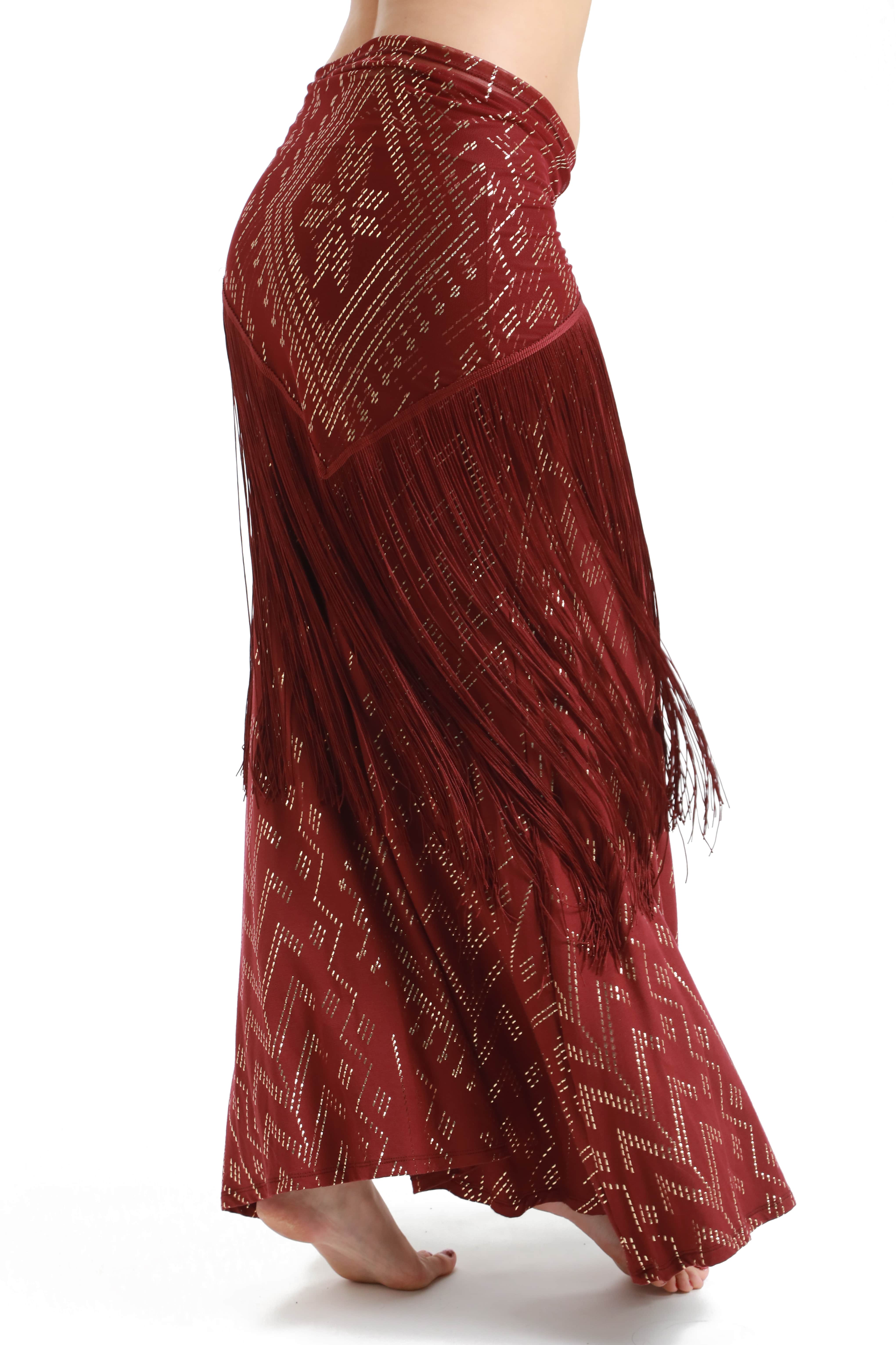 A person wearing the Melodia Designs Fringe Shimmy Shawl Luxor, featuring maroon geometric patterns and silky chainette fringe, stands barefoot against a white background—a striking festival fashion statement.