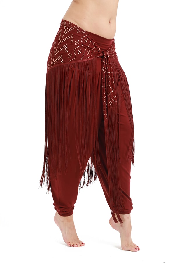 A person stands barefoot against a white background, wearing maroon harem pants with Melodia Designs Fringe Shimmy Shawl Luxor—a matching hip scarf adorned with silky chainette fringe, perfect as a festival fashion statement piece.