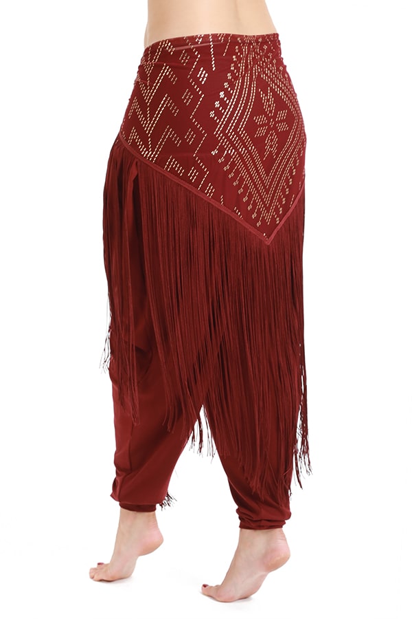 A person models the Melodia Designs Fringe Shimmy Shawl Luxor, featuring maroon fabric with silky chainette fringe and a geometric gold pattern—shown waist down and barefoot on white. Perfect as a statement piece for festivals.