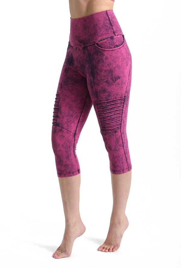 A person wears Melodia Designs Moto Capri 2.0 Grunge Tourmaline—high-waisted, cropped pink eco-luxe leggings with ribbed moto detailing above the knees—standing barefoot against a plain white background.