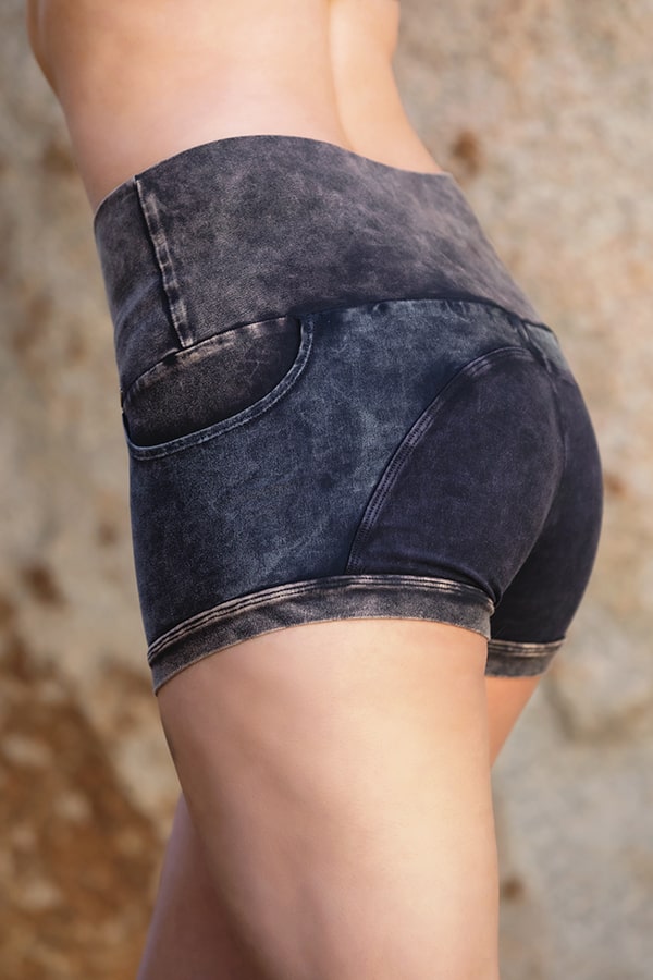 Someone is shown from the waist down, standing sideways against a blurred background, wearing Melodia Designs Moto Short Grunge—high-waisted, dark shorts made from eco-luxe fabric.