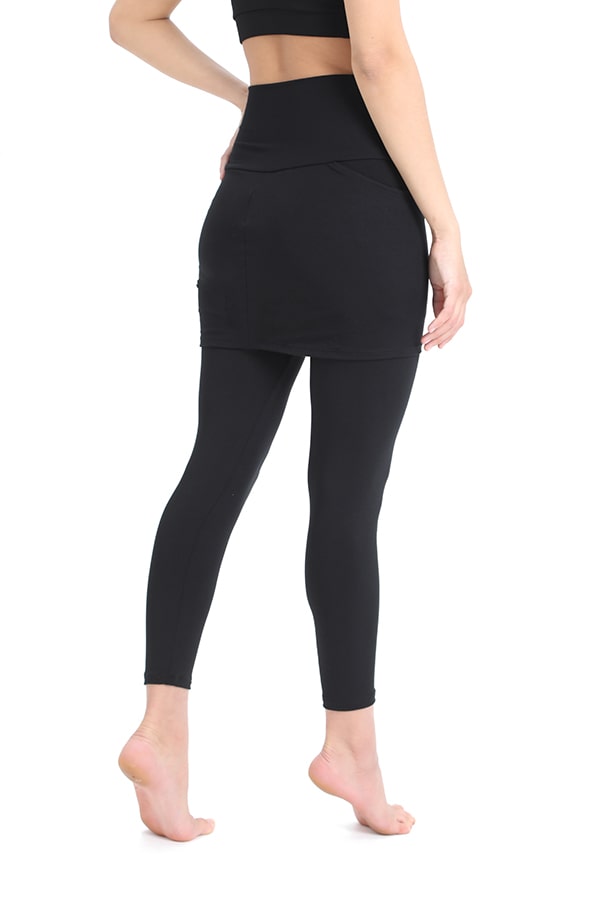 A person is shown from the back, barefoot, wearing Melodia Designs’ Sharon Skirted Pocket Legging in eco-luxe Modal and a black crop top, standing against a white background.