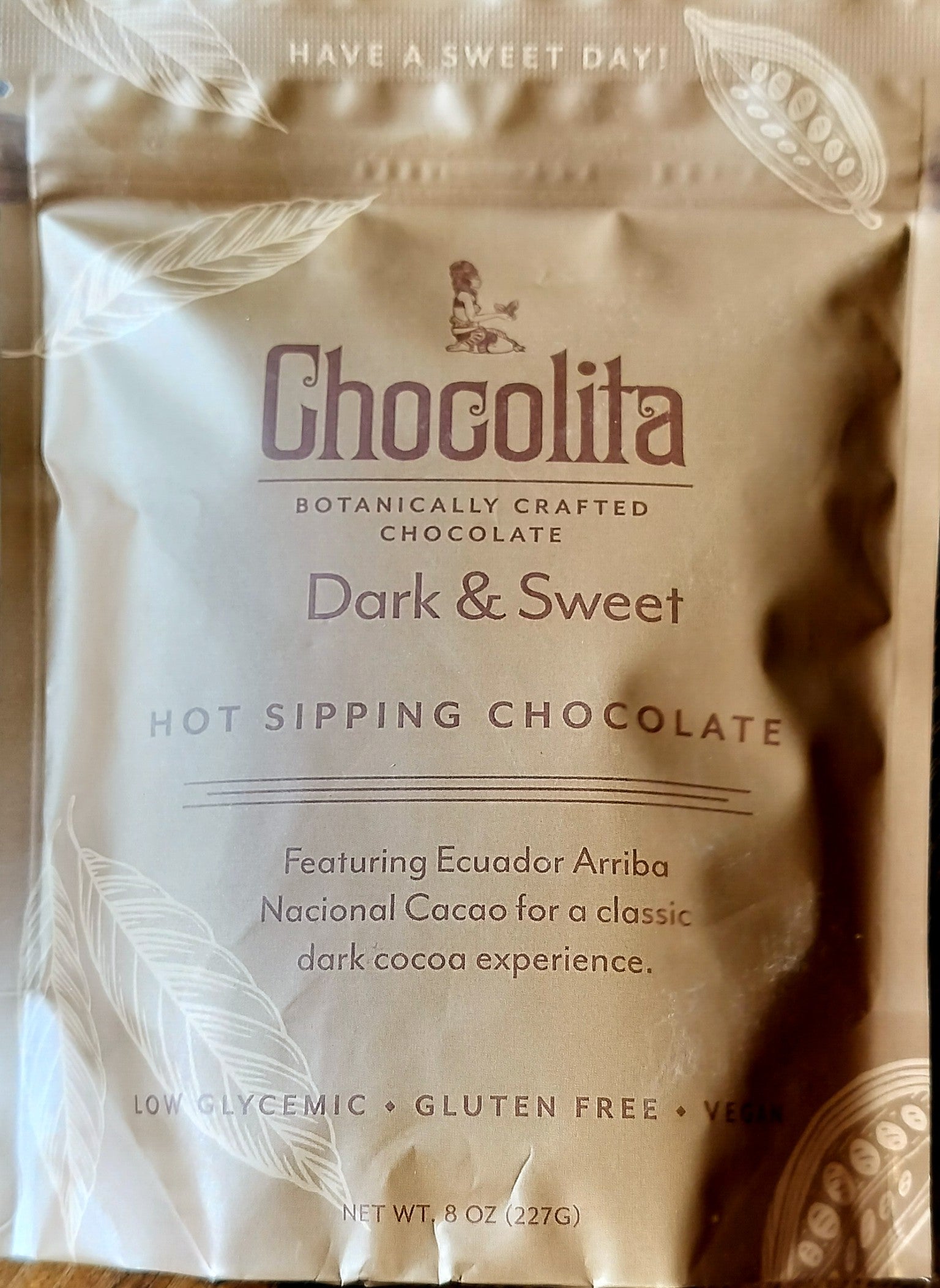 A metallic brown pouch labeled chocolita.com Dark & Sweet Sipping Chocolate with Ecuadorian Arriba Nacional Cacao. Botanically crafted, low glycemic, gluten-free, and vegan—ideal for sipping chocolate lovers.