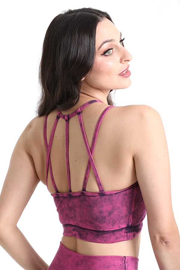 A woman with long dark hair models the Melodia Designs Aeon Bra Grunge Rhodonite, a purple tie-dye strappy back crop top, shown from behind and looking over her shoulder. Eco-luxe fabric ensures comfort and style.