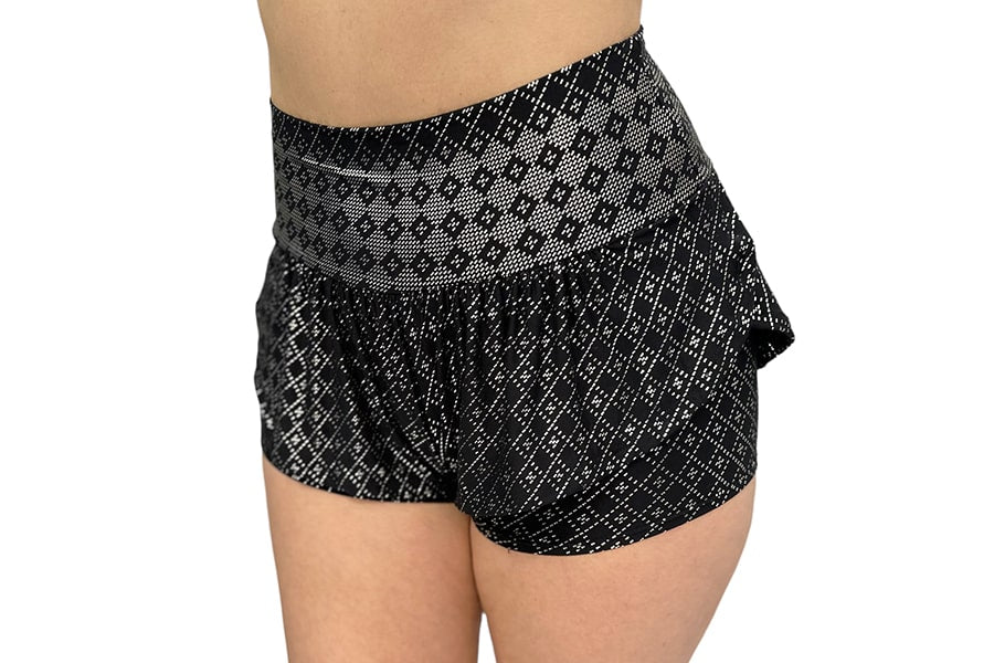 A person wears Melodia Designs’ Angela Ruffle Short—black, high-waisted athletic shorts with a white diamond pattern and an elastic-free waistband—while standing against a white background.