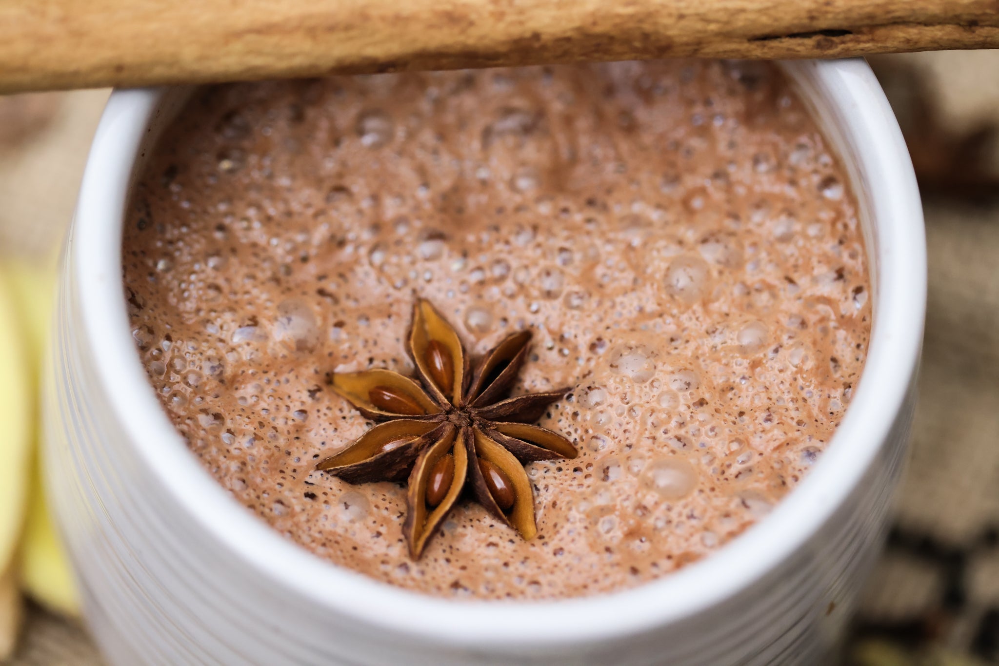 A close-up of chocolita.coms Chaga & Chai Sipping Chocolate, frothy and topped with star anise and a cinnamon stick on the rim.