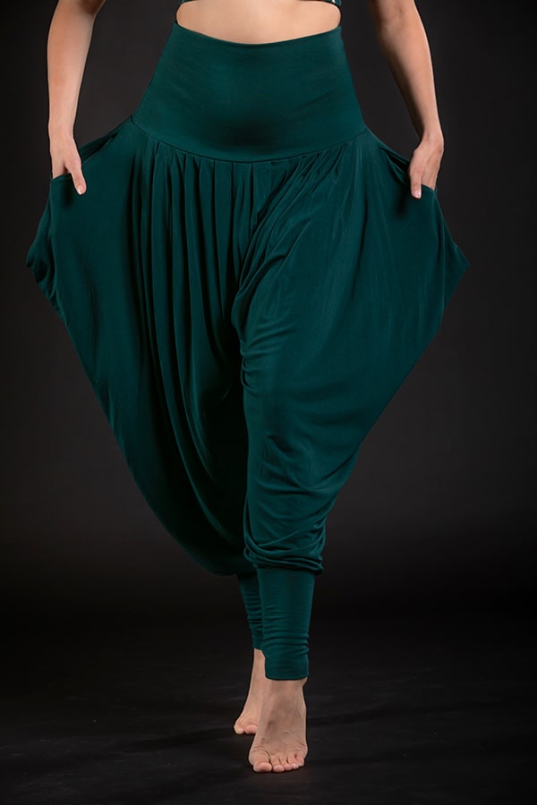 A person models Melodia Designs’ Jazmine Harem Pant Malachite, barefoot against a black background, showing off the loose fit, wide draped legs, deep side pockets, and fold-over waistband.