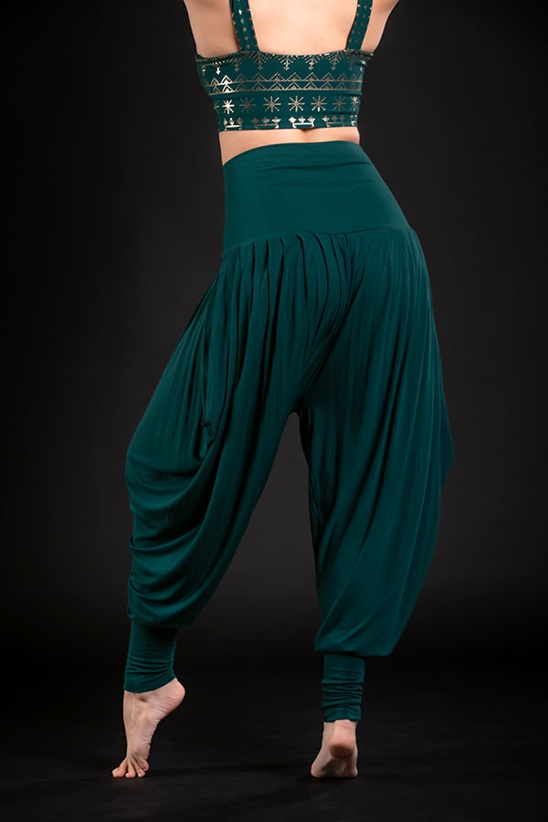 A person wearing Melodia Designs Jazmine Harem Pant Malachite with deep side pockets and a matching embroidered crop top stands barefoot on tiptoe against a black background, facing away from the camera.